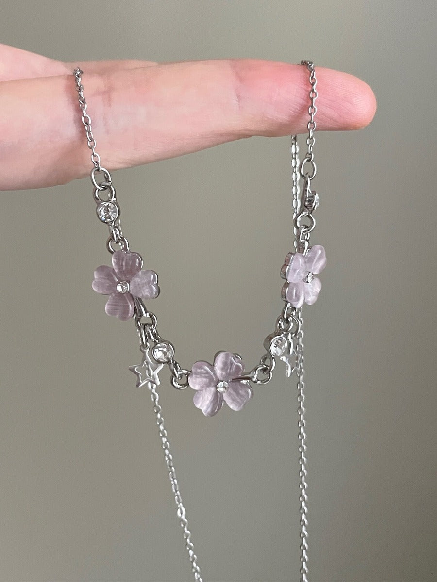 Necklace with floral pendants held between fingers against a neutral background