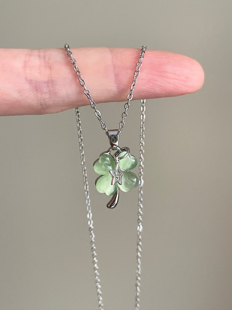 Necklace with a green clover pendant held between fingers against a neutral background