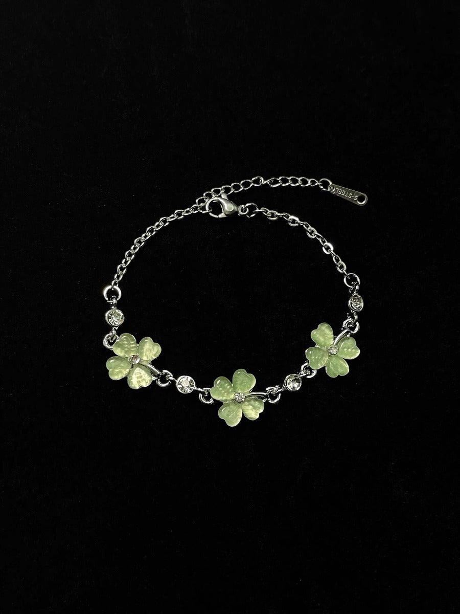 Silver bracelet with green clover-shaped charms on a black background