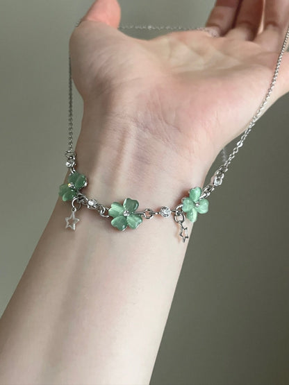 Hand wearing a delicate bracelet with green floral charms on a neutral background