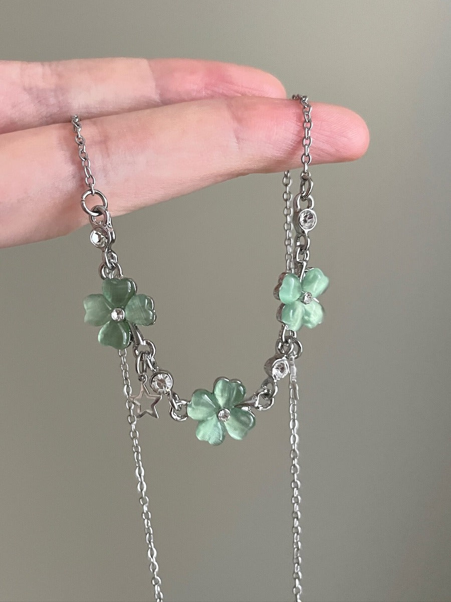 Necklace with green flower pendants held between fingers against a neutral background