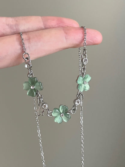 Necklace with green flower pendants held between fingers against a neutral background