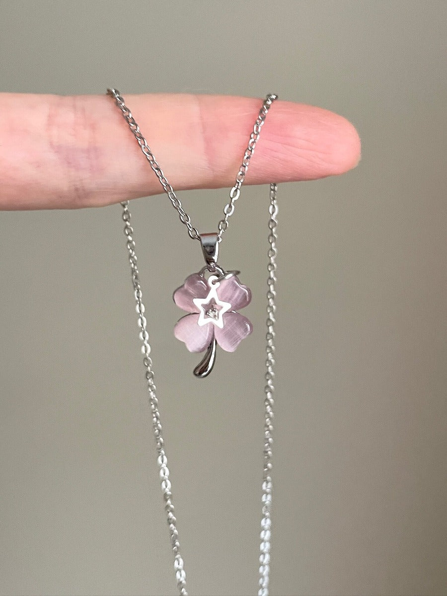 Necklace with a pink flower pendant held between fingers against a neutral background