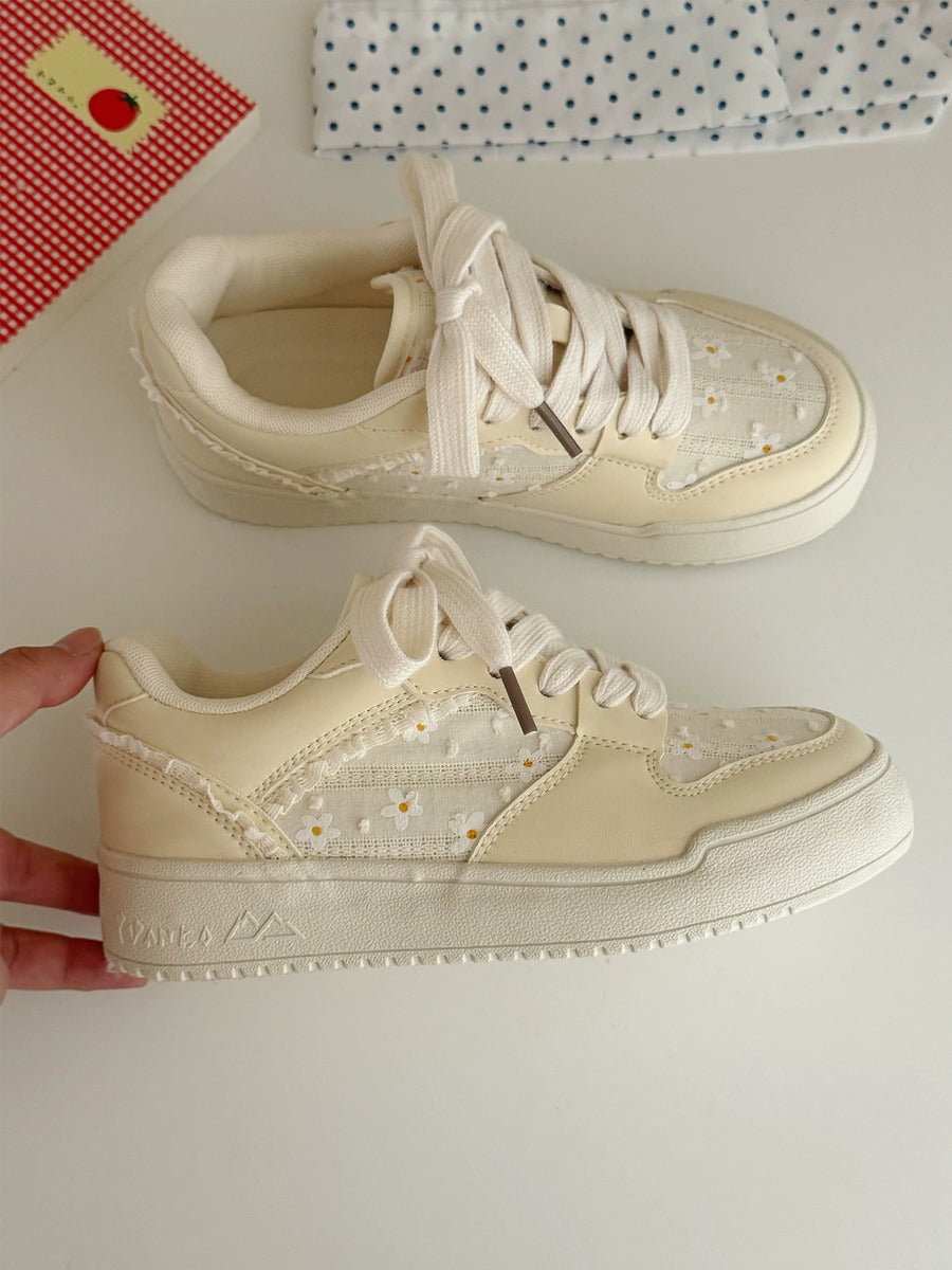 Pair of beige sneakers with white laces on a light surface.