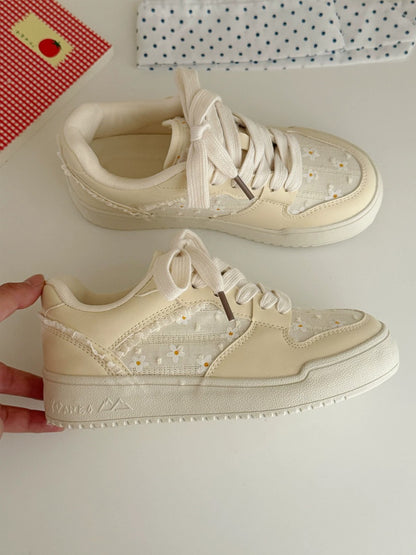 Pair of beige sneakers with white laces on a light surface.