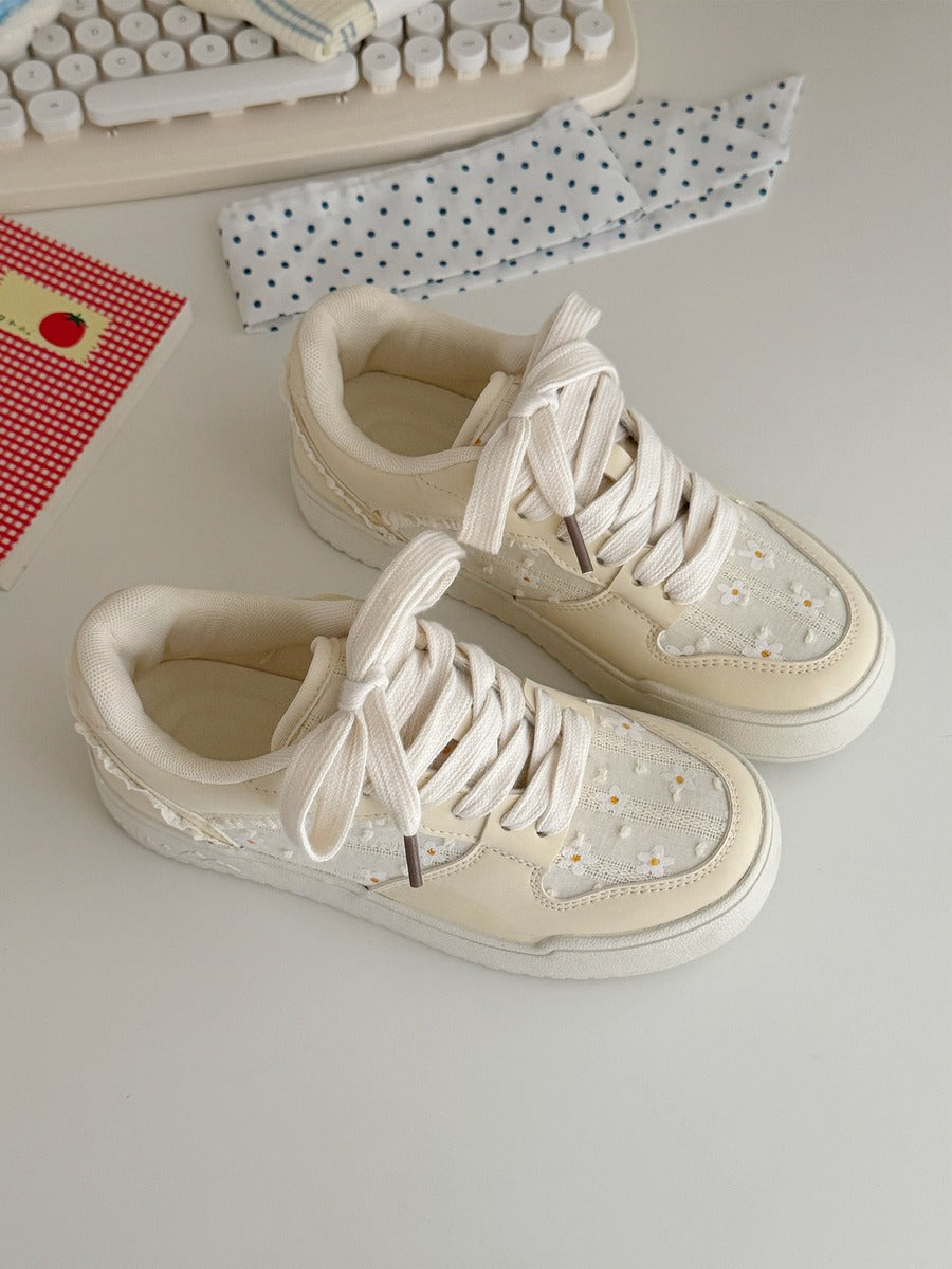 Pair of cream-colored sneakers on a light surface with a keyboard and paper in the background.