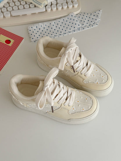 Pair of cream-colored sneakers on a light surface with a keyboard and paper in the background.