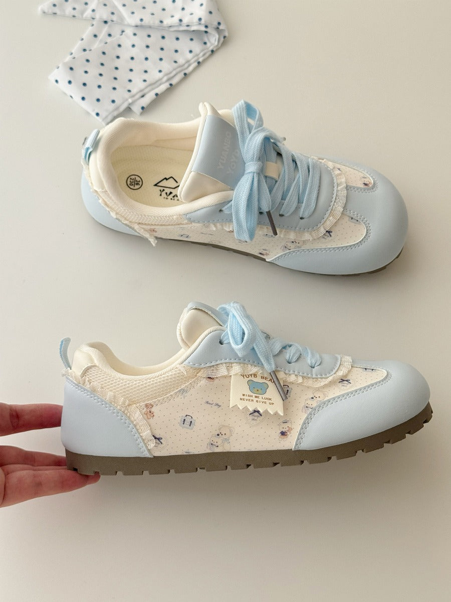 Pair of light blue and beige sneakers with decorative bows on a neutral background