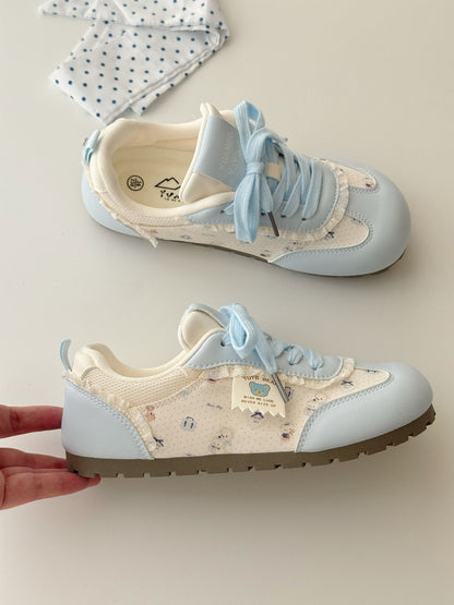 Pair of light blue and beige sneakers with decorative bows on a neutral background
