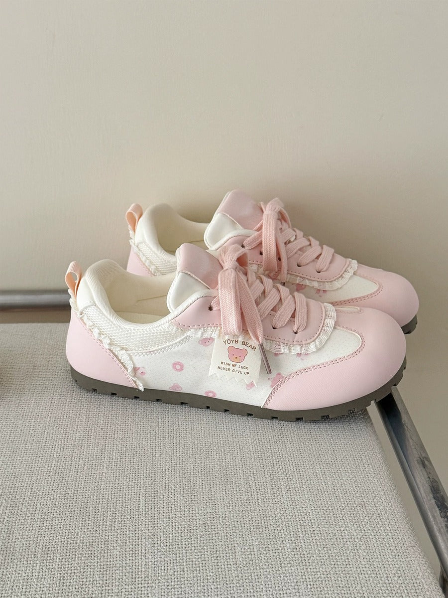 Pair of pink sneakers with white laces on a light gray surface.