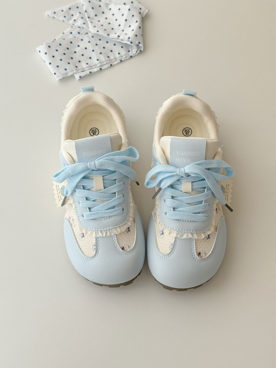 Pair of light blue children's sneakers with white laces on a neutral background