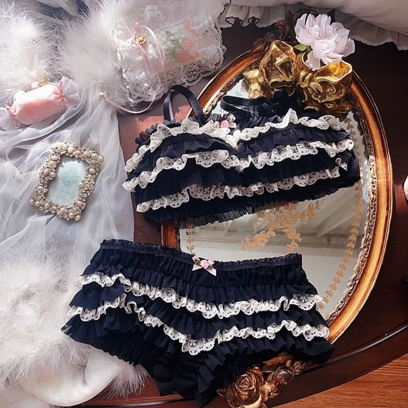 Black lace baby bloomers on a decorative surface with flowers and ribbons.