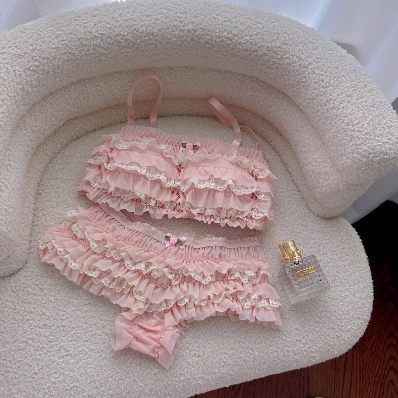 Pink ruffled lingerie set with a bottle of perfume on a textured surface.