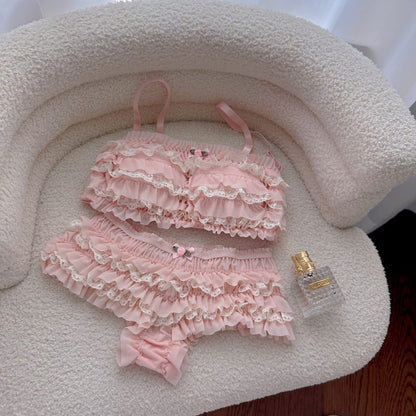Pink ruffled lingerie set with a bottle of perfume on a textured surface.