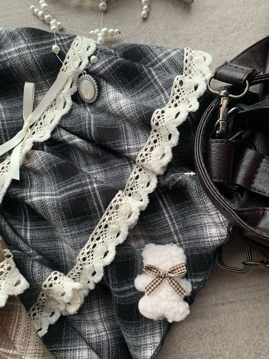 Plaid fabric with lace trim and a small white teddy bear toy on a textured surface.