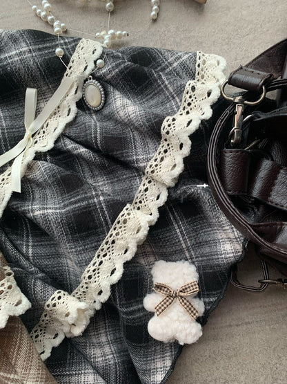 Plaid fabric with lace trim and a small white teddy bear toy on a textured surface.