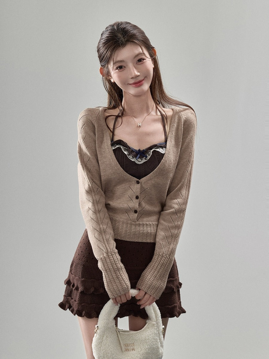 A woman modeling a beige long-sleeve knit cardigan over a black lace-trimmed top, paired with a brown ruffled skirt and holding a cream-colored handbag against a plain light gray studio background.