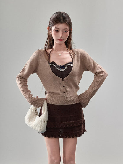 A woman modeling a beige cardigan sweater over a dark brown lace-trimmed camisole, paired with a dark brown mini skirt and holding a white textured handbag, against a solid light gray studio background.