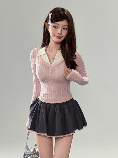 A young woman modeling a pink ribbed knit long-sleeve top with a cream collar, paired with a dark gray pleated mini skirt, against a plain light gray studio background.
