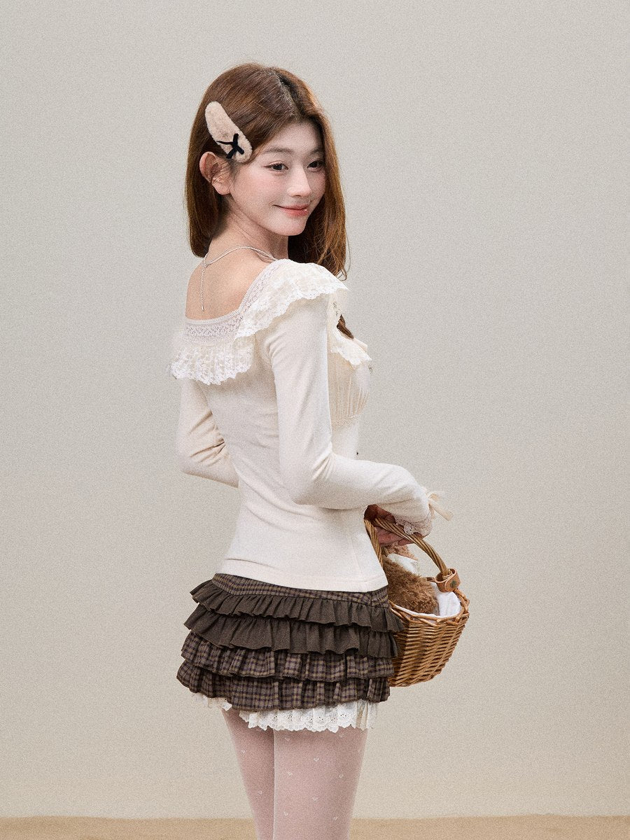 A young woman posing in a cream off-the-shoulder long-sleeve top with lace trim, a brown tiered ruffle mini skirt, and pink tights, holding a small wicker basket against a plain beige background.
