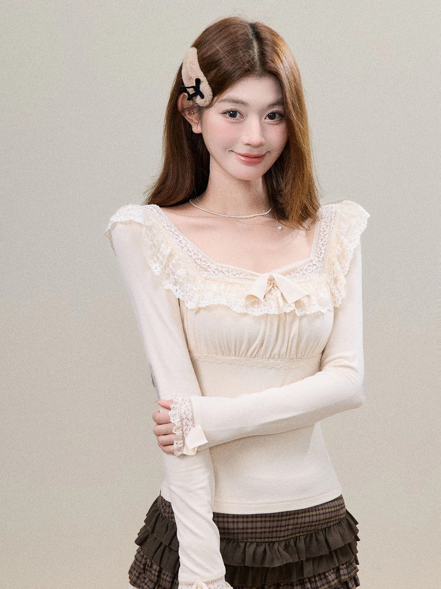 A young woman modeling a cream-colored long-sleeve top with delicate lace ruffles and a sweetheart neckline, paired with a brown ruffled skirt, against a plain light gray background.
