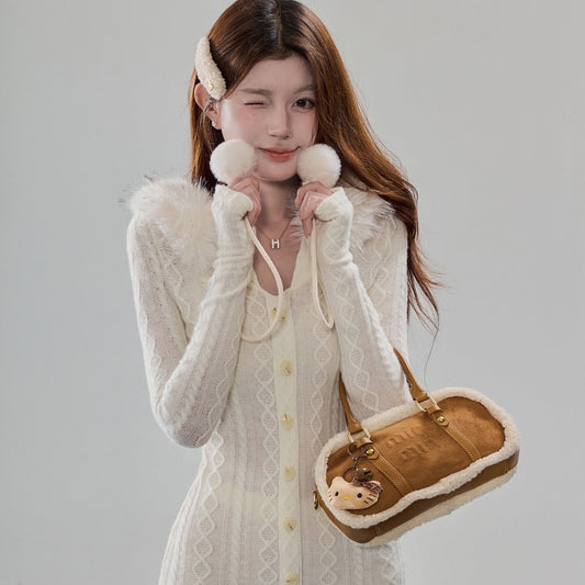 A woman models a cream-colored cable-knit cardigan dress with fluffy faux-fur trim at the collar and cuffs, paired with matching knit gloves and a brown and cream plush handbag.