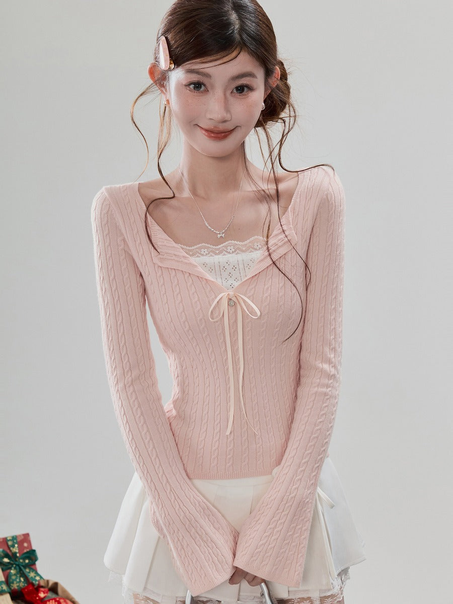 A young woman wearing a light pink ribbed knit long-sleeve top with a square neckline, white lace trim, and a small front tie detail, paired with a white skirt against a plain light gray studio background.