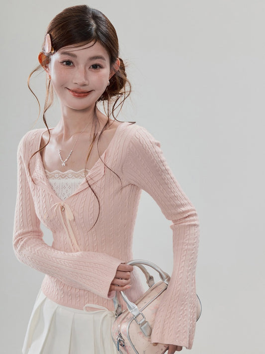 A woman wearing a light pink cable-knit cardigan over a white lace-trimmed top, holding a matching light pink handbag against a plain light gray studio background.