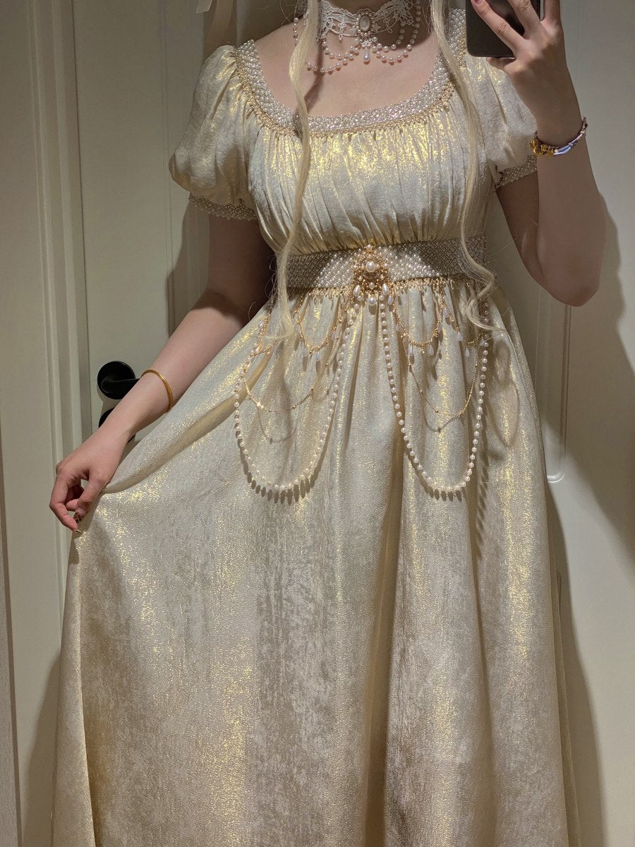 Person wearing a gold and white dress with decorative elements, standing against a neutral background.