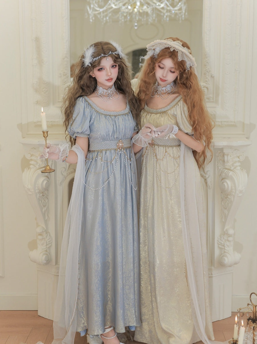 Two dolls in vintage-style dresses standing in a decorative room with a chandelier.
