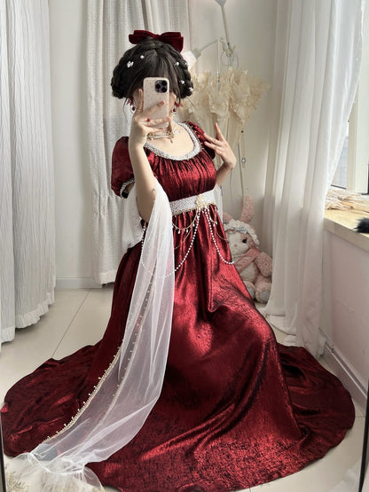 Person wearing a red dress with a white train in a room with white curtains and a teddy bear.