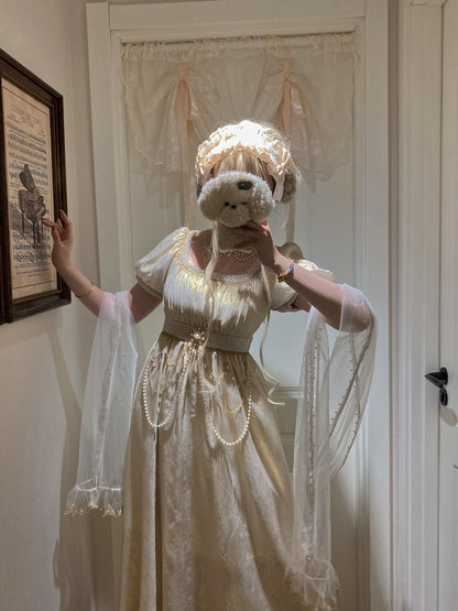 Person in a white dress holding a teddy bear in a room with a framed picture on the wall.
