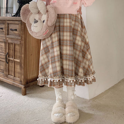 A girl wearing a plaid skirt with pom-pom trim, white socks, and fluffy shoes in a room.