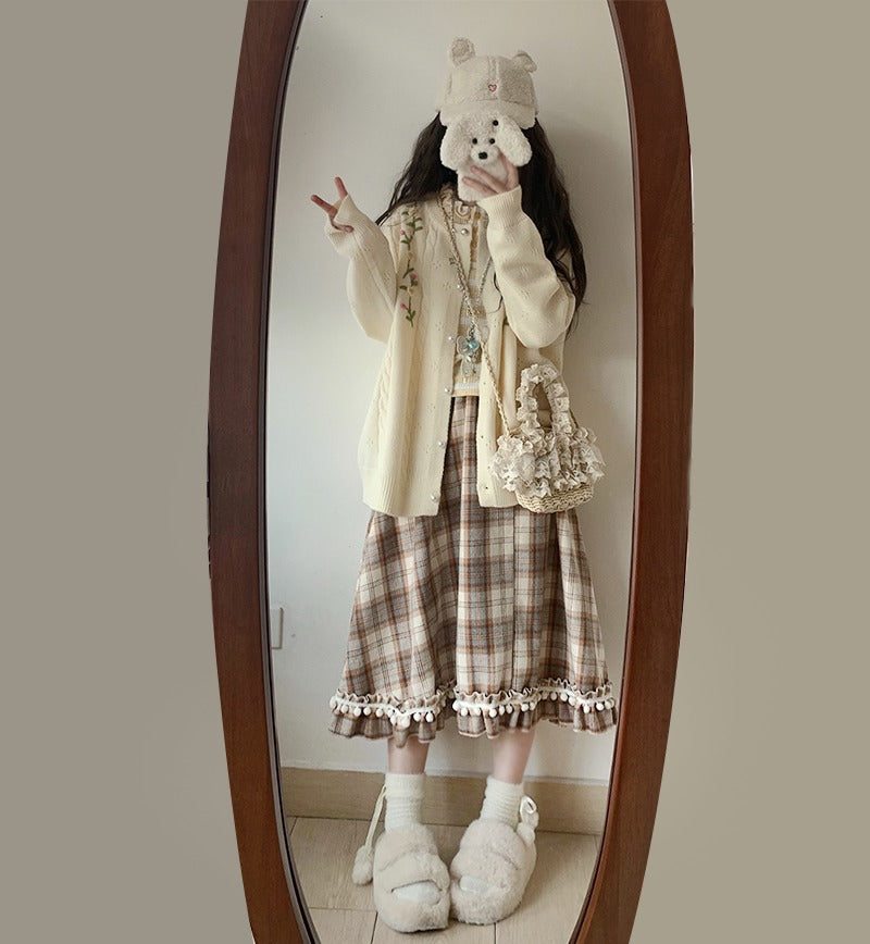 Person wearing a cream cardigan, plaid skirt, and white slippers in front of a mirror.