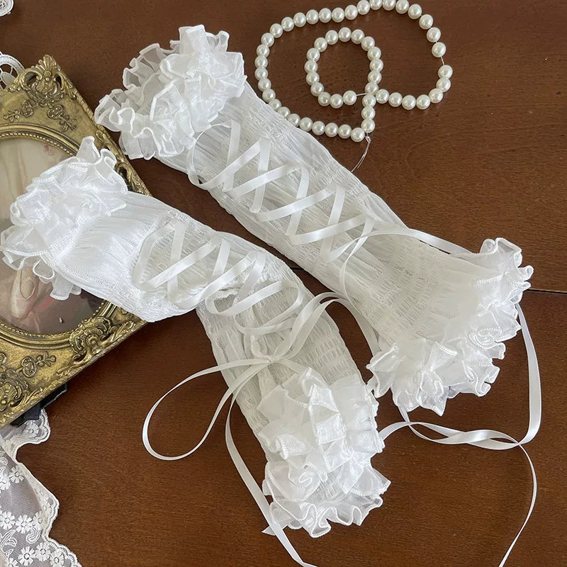 White lace gloves with ruffles on a wooden surface with a pearl necklace and decorative frame.