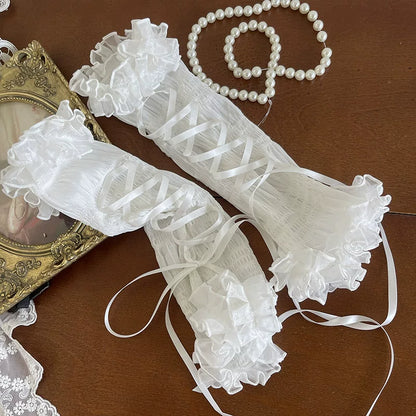 White lace gloves with ruffles on a wooden surface with a pearl necklace and decorative frame.