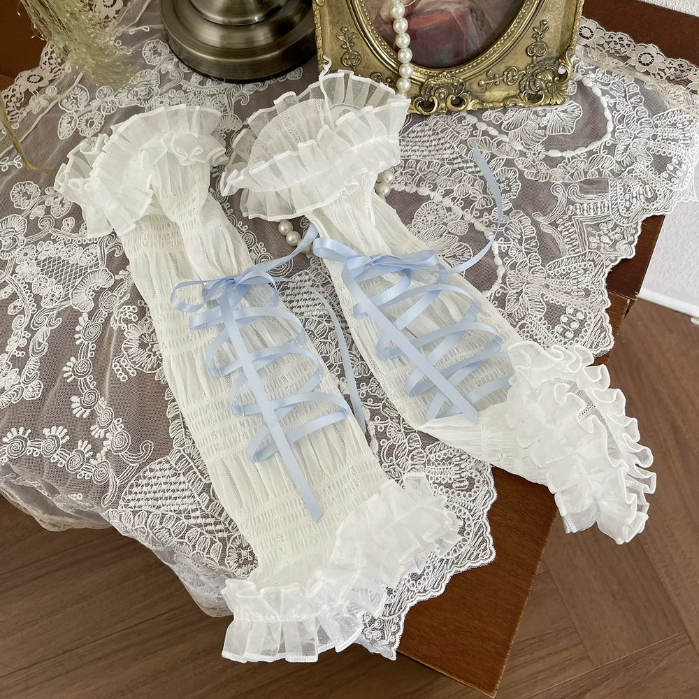 Pair of lace gloves with blue ribbons on a lace tablecloth.