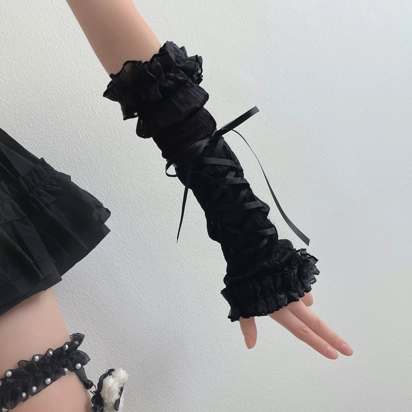 Black ruffled wrist cuffs on a person against a light gray background