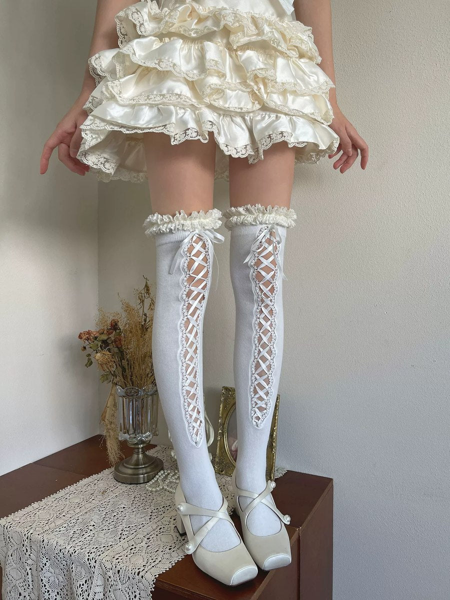 Person wearing a white lace dress, stockings, and shoes on a wooden surface with a neutral background.