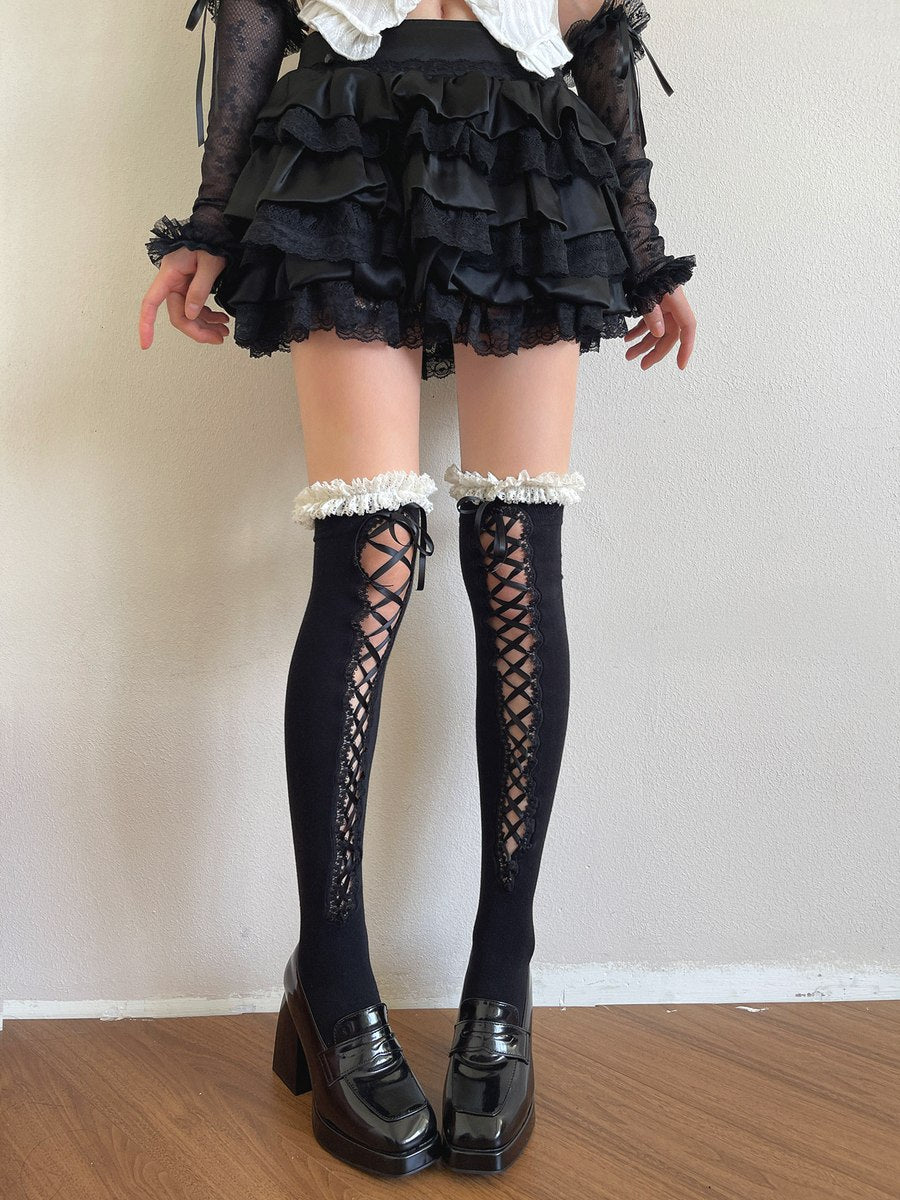 Person wearing a black ruffled skirt, black knee-high boots with lace-up design, and white stockings.