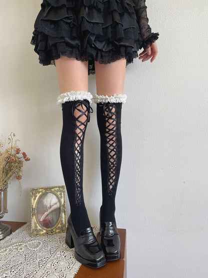 Person wearing black lace-up knee-high socks with a white trim, standing against a neutral background.