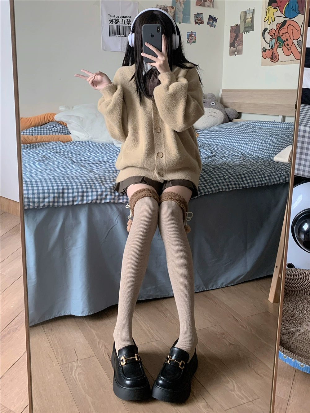 Person taking a mirror selfie wearing a beige cardigan, black shoes, and white tights in a bedroom.