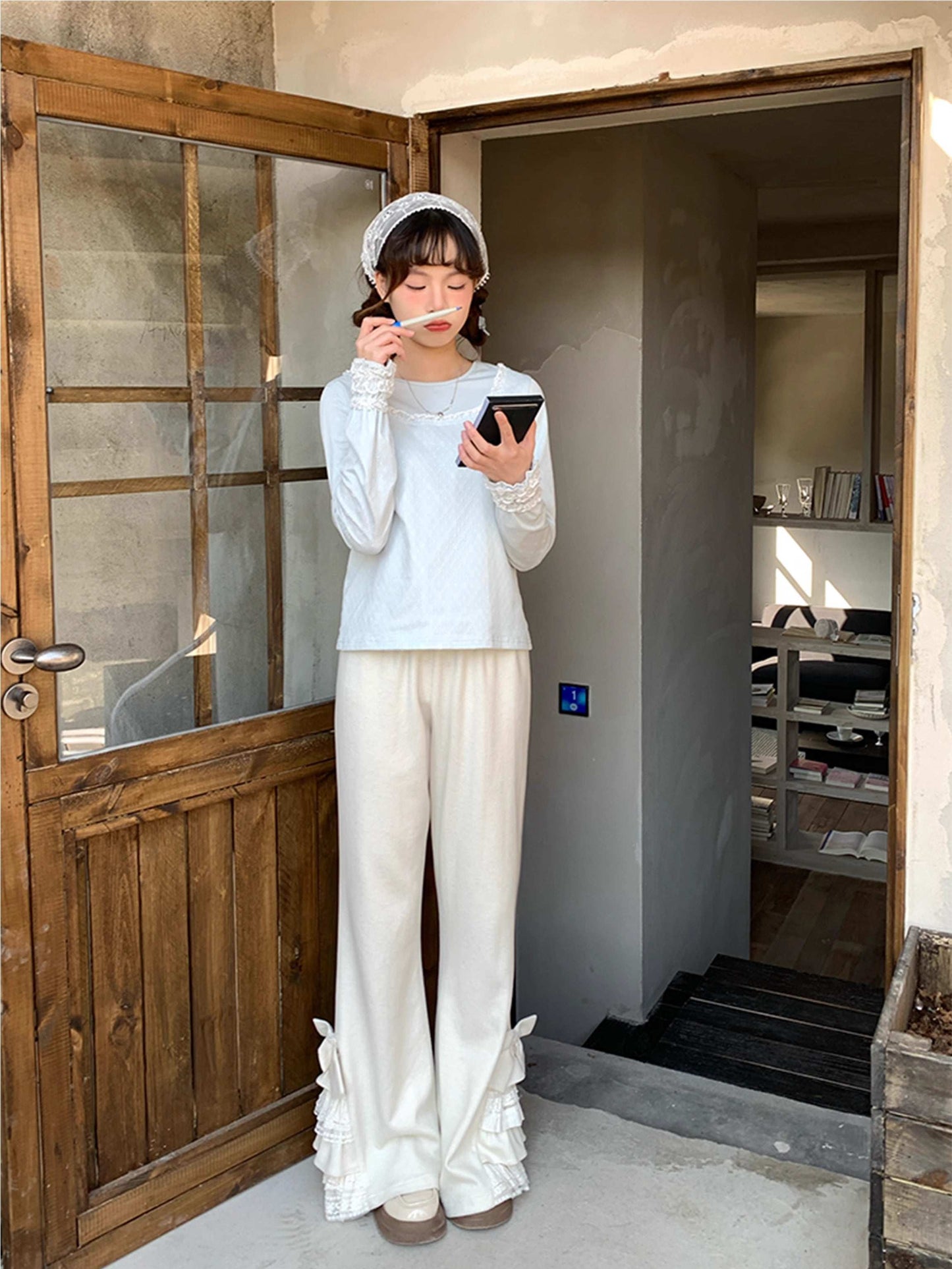 Person in white pants standing in a doorway, holding a phone and eating.