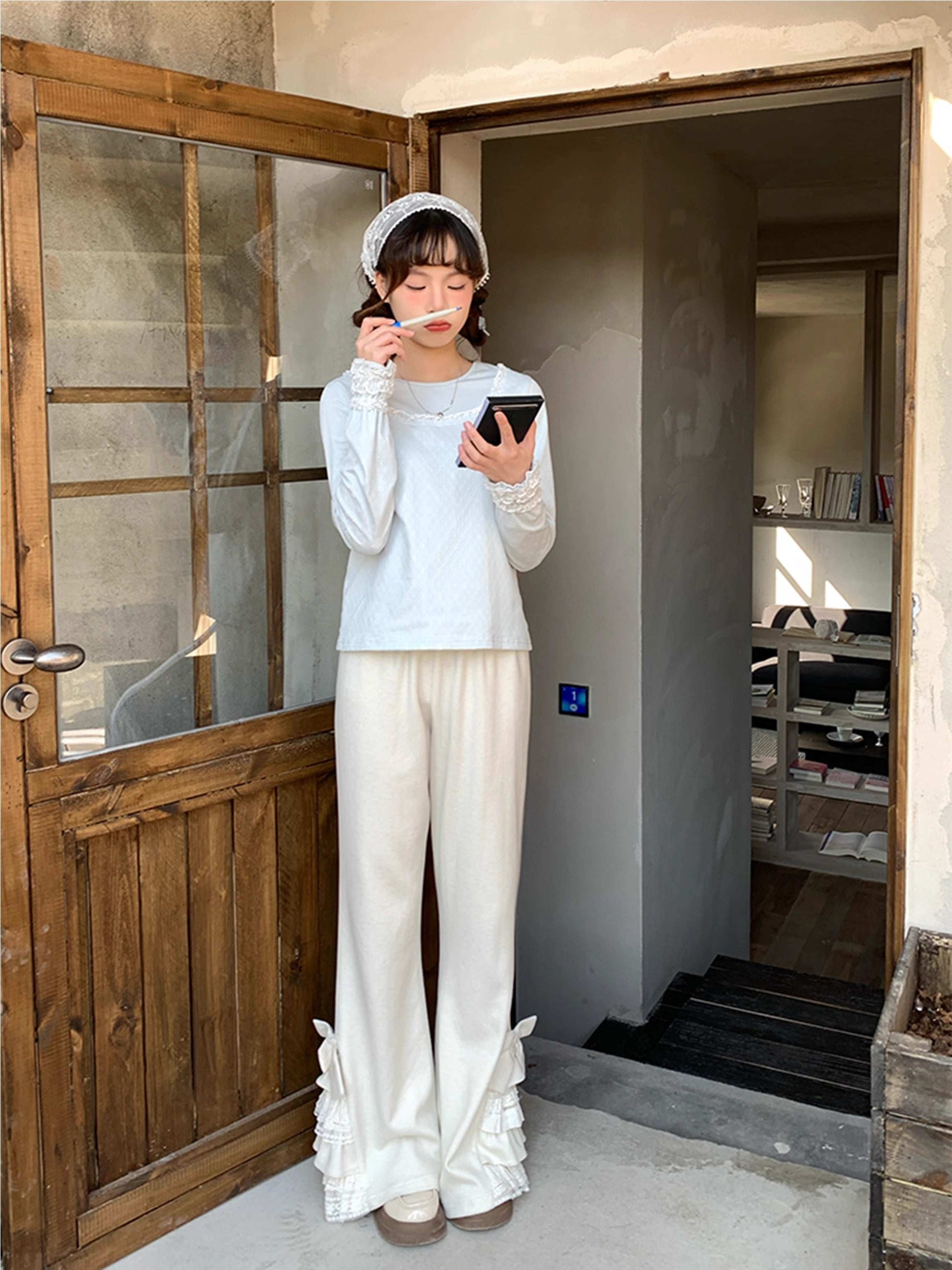 Person in white pants standing in a doorway, holding a phone and eating.