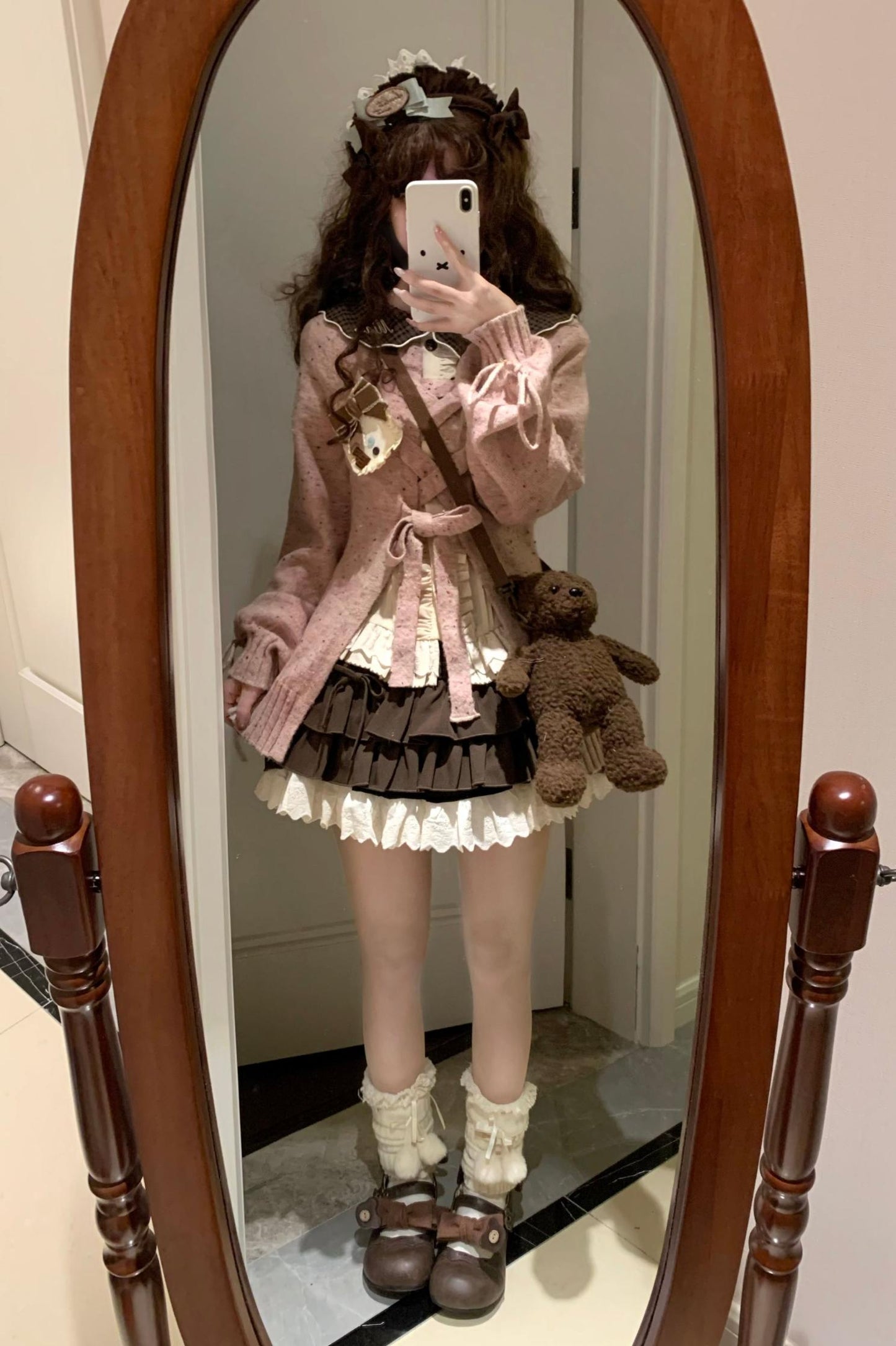 Person in a pink outfit with a teddy bear standing in front of a mirror.