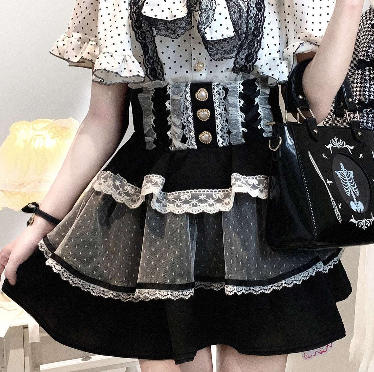 Person wearing a jirai kei black and white polka dot dress with lace details, holding a black handbag.