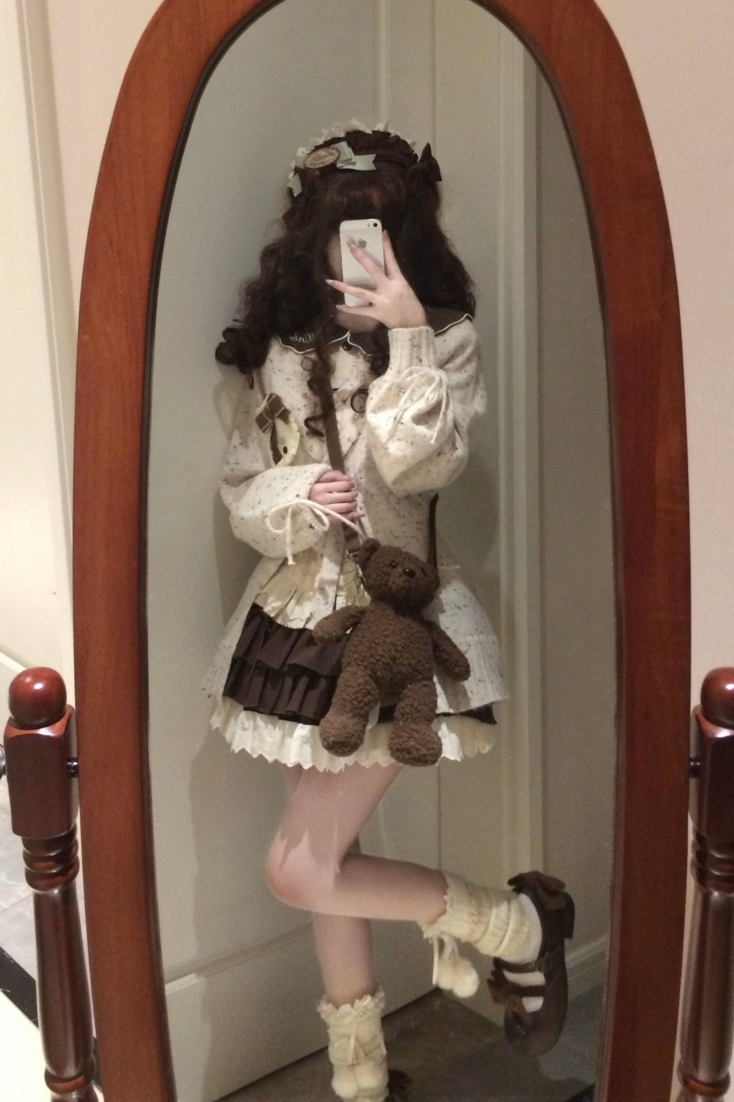Person in a white dress with ruffles holding a teddy bear, standing in front of a mirror.