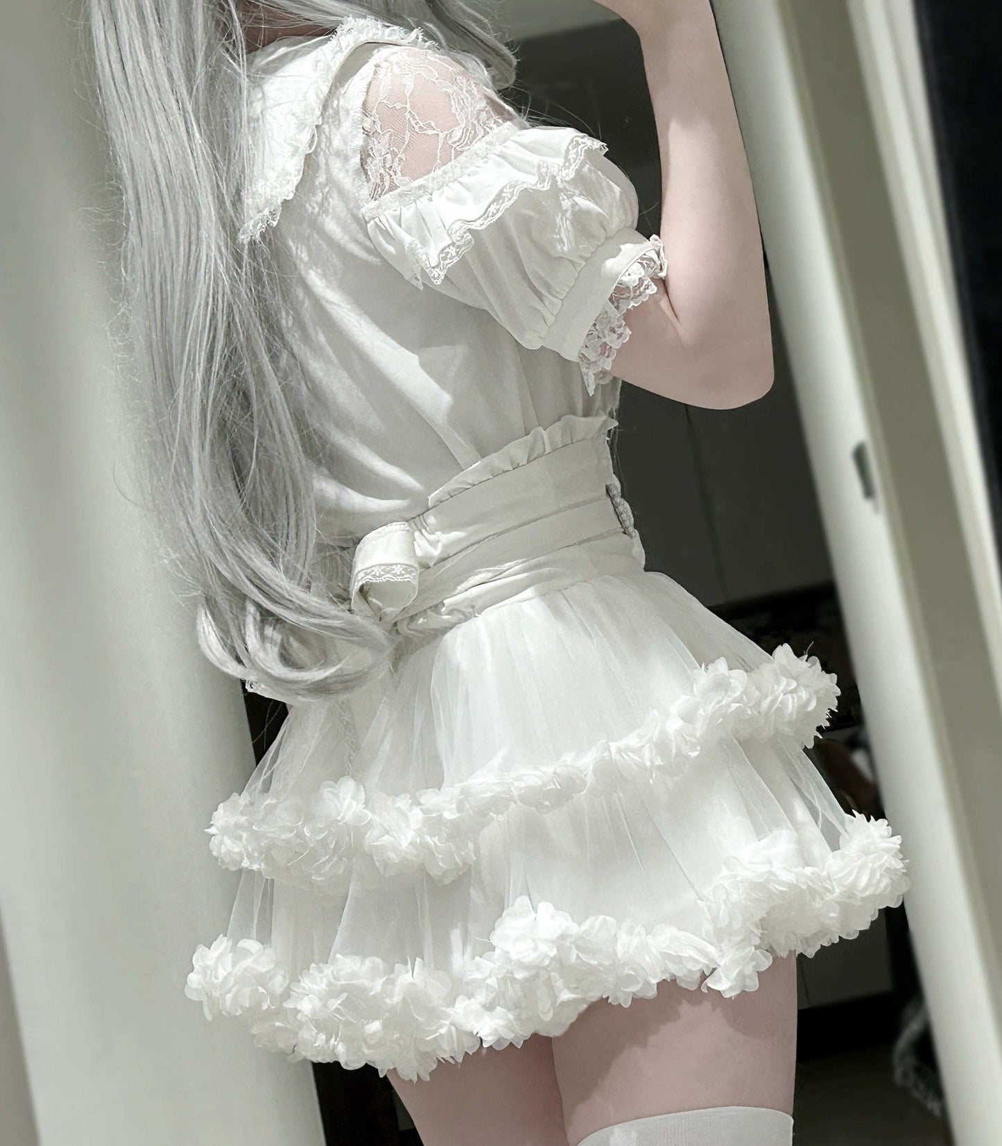 Person wearing a white lace dress with a fluffy skirt, standing indoors.