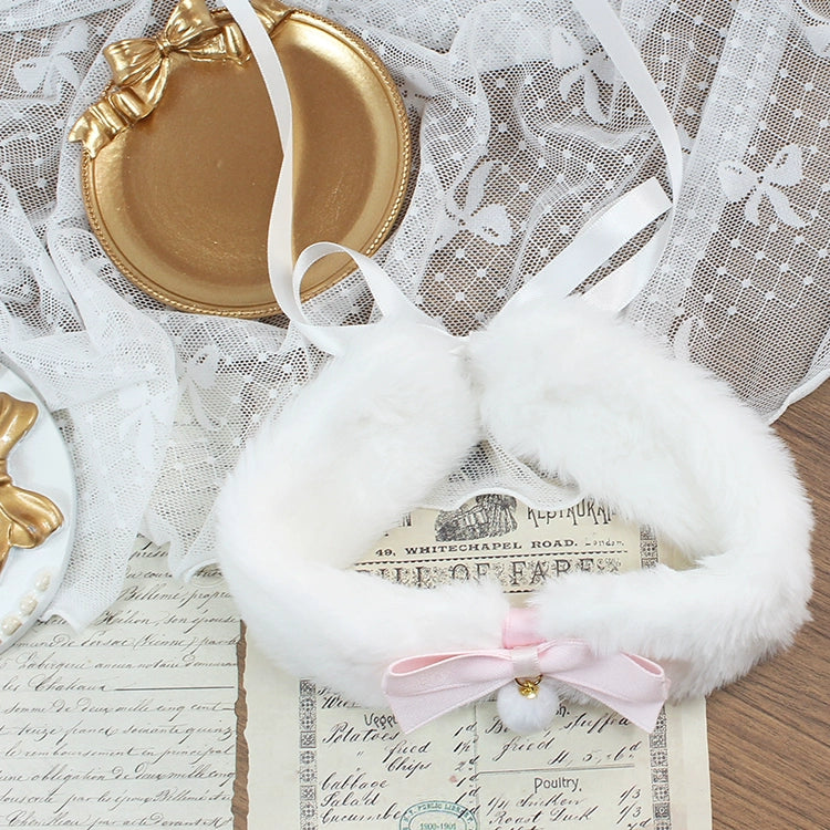 White furry collar with a pink bow on a textured surface with lace and paper.