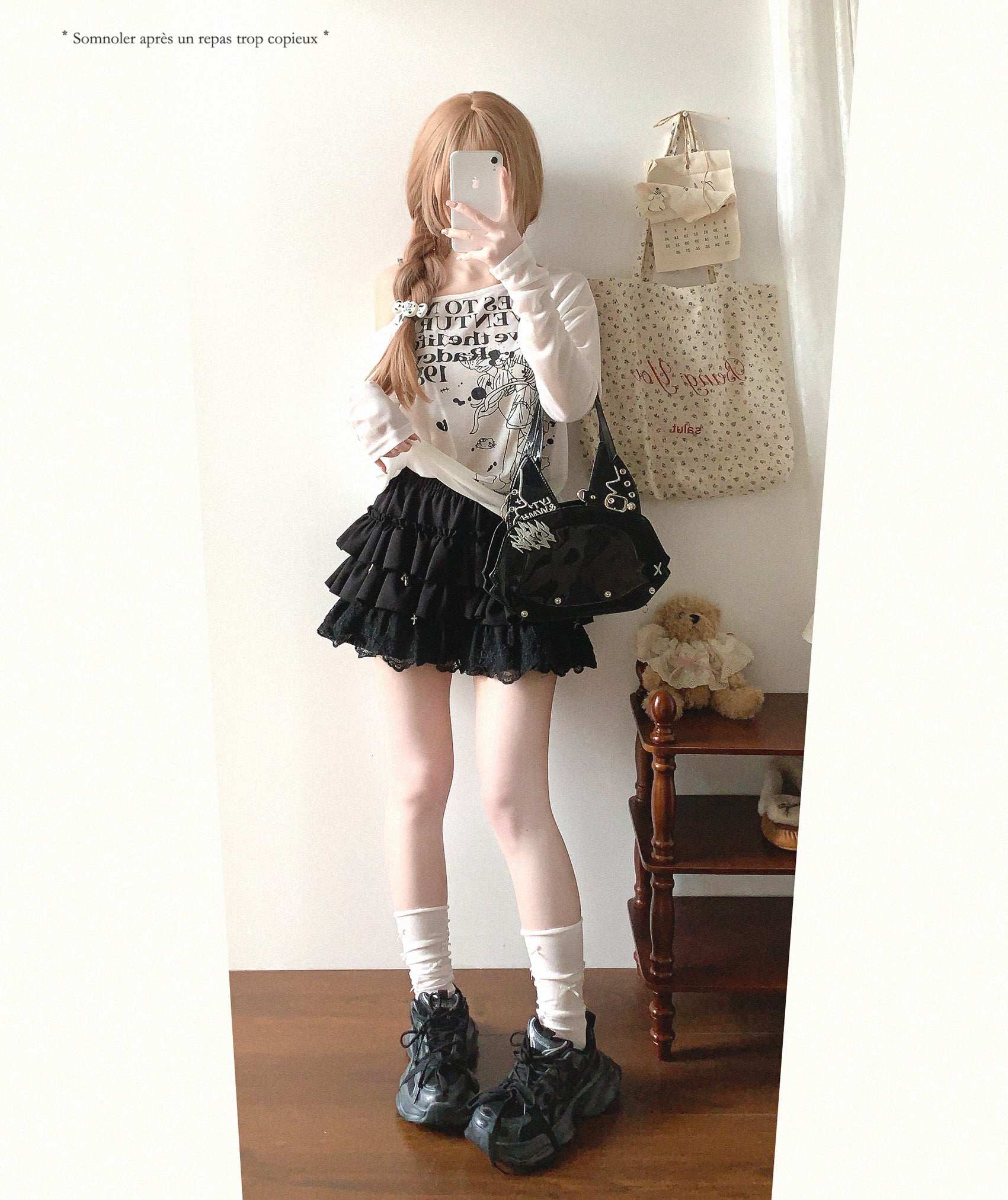 Person wearing a black skirt and white top in a room with a teddy bear and bags.